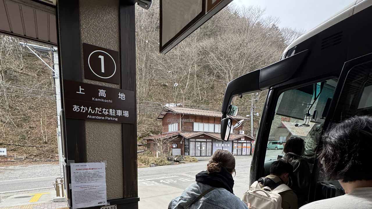 ภาพผู้โดยสารกำลังขึ้นรถบัสที่ป้ายหมายเลข 1 เพื่อเดินทางไปคามิโคจิ (Kamikochi) หรือสถานีปลายทาง โดยมีฉากหลังเป็นอาคารไม้และป่าในช่วงต้นฤดูใบไม้ผลิ แสดงถึงจุดต่อรถขนส่งสำคัญ