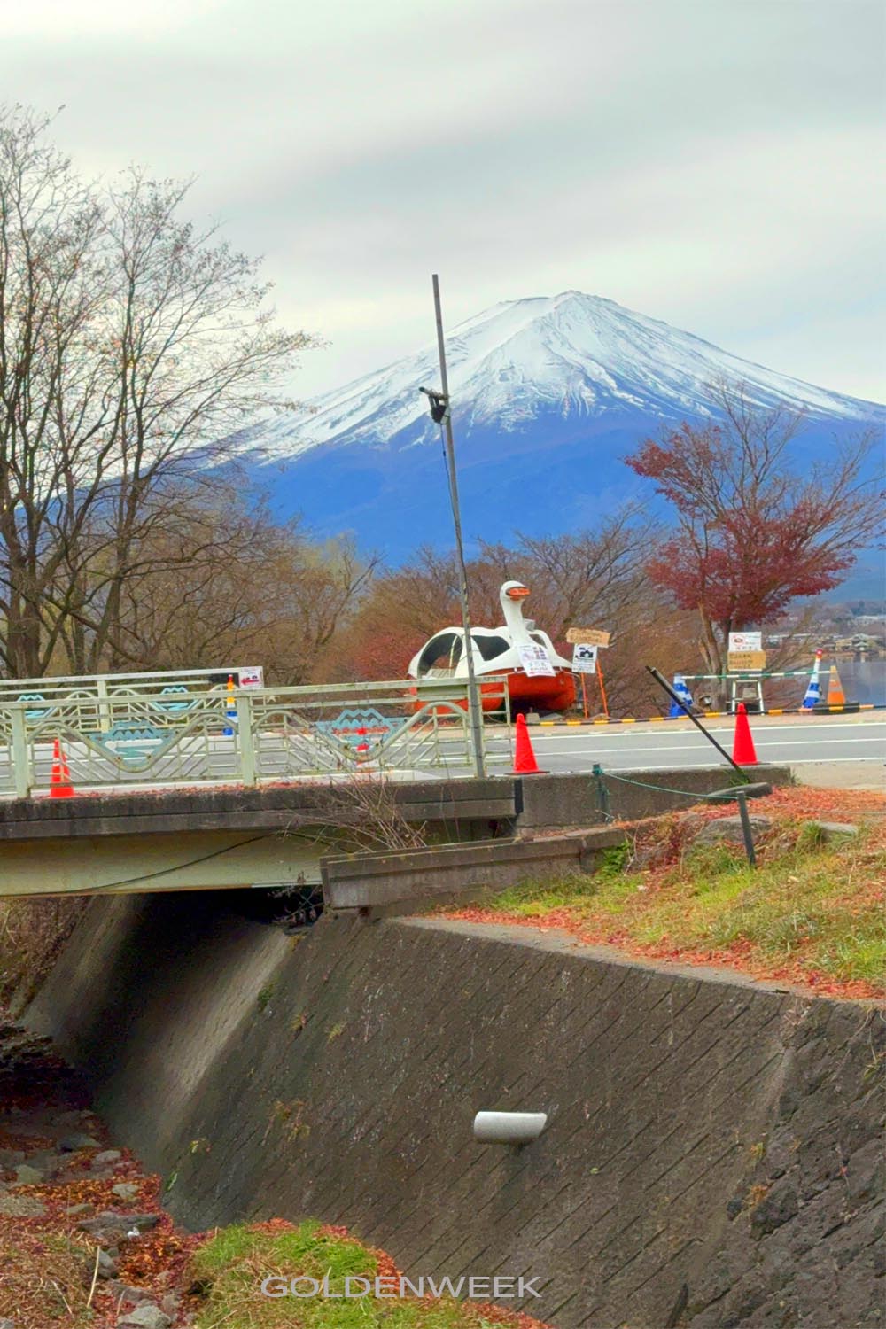 ภูเขาไฟฟูจิปกคลุมด้วยหิมะเป็นฉากหลังของสะพานและถนนใกล้ Kawaguchiko ในฤดูใบไม้ร่วง