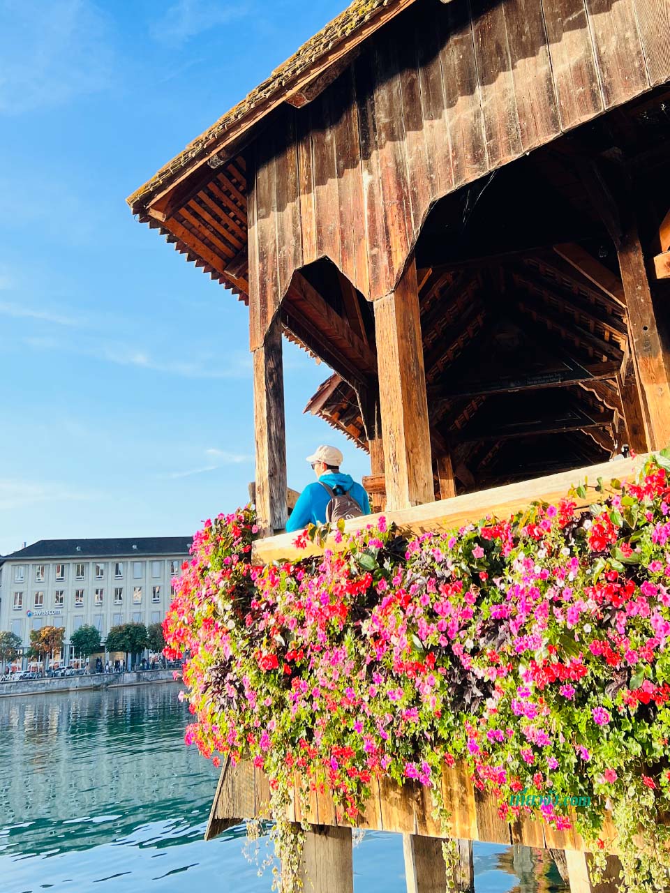 สะพานไม้ Kapellbrücke ทอดยาวข้ามแม่น้ำรอยส์ ประดับด้วยดอกไม้สีสดใส โดยมีหอคอย Water Tower และยอดเขาเป็นฉากหลัง
